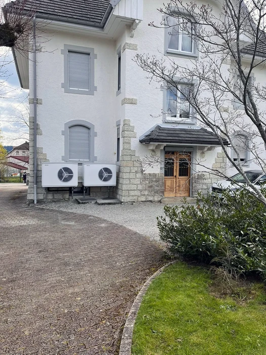 Extérieur résidentiel avec maison blanche à volets gris, entrée principale en bois sous auvent