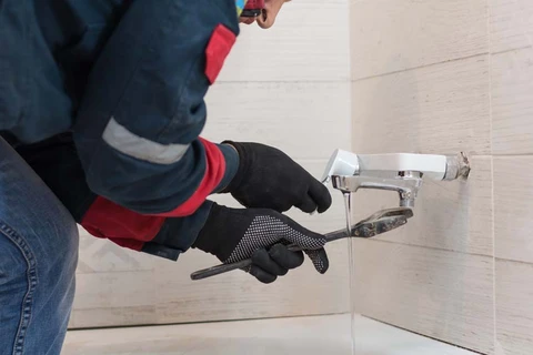 Plombier professionnel en combinaison de travail installant un robinet mural dans salle de bain carrelée blanche
