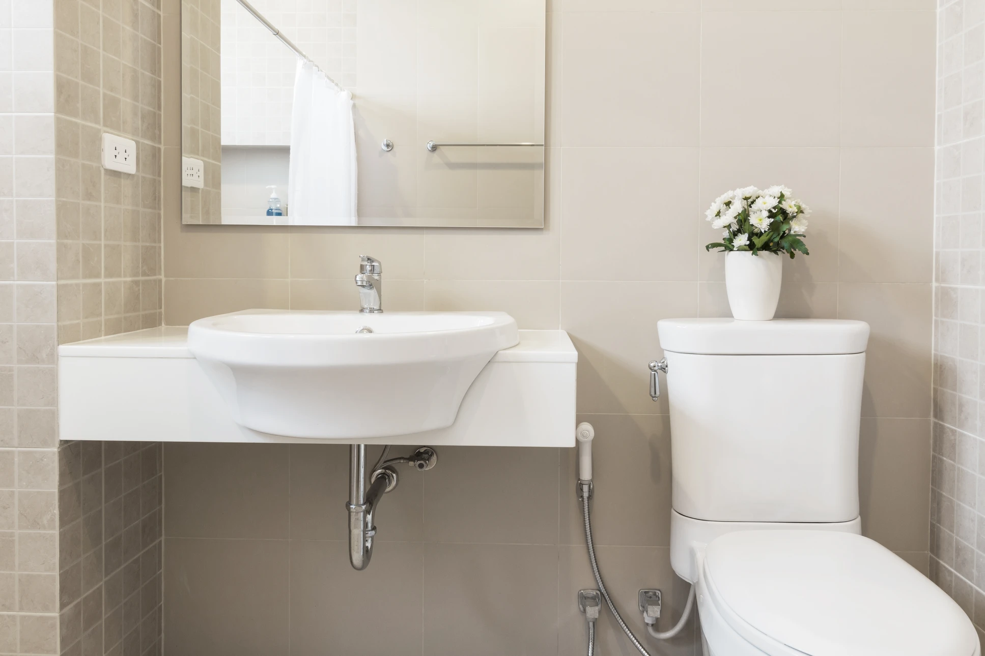 Salle de bain moderne avec carrelage beige, lavabo suspendu blanc à robinet chromé, WC deux pièces avec réservoir haut