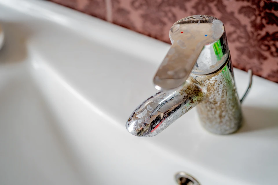 Salle de bain avec robinet de lavabo en chrome présentant des dépôts calcaires et traces de corrosion
