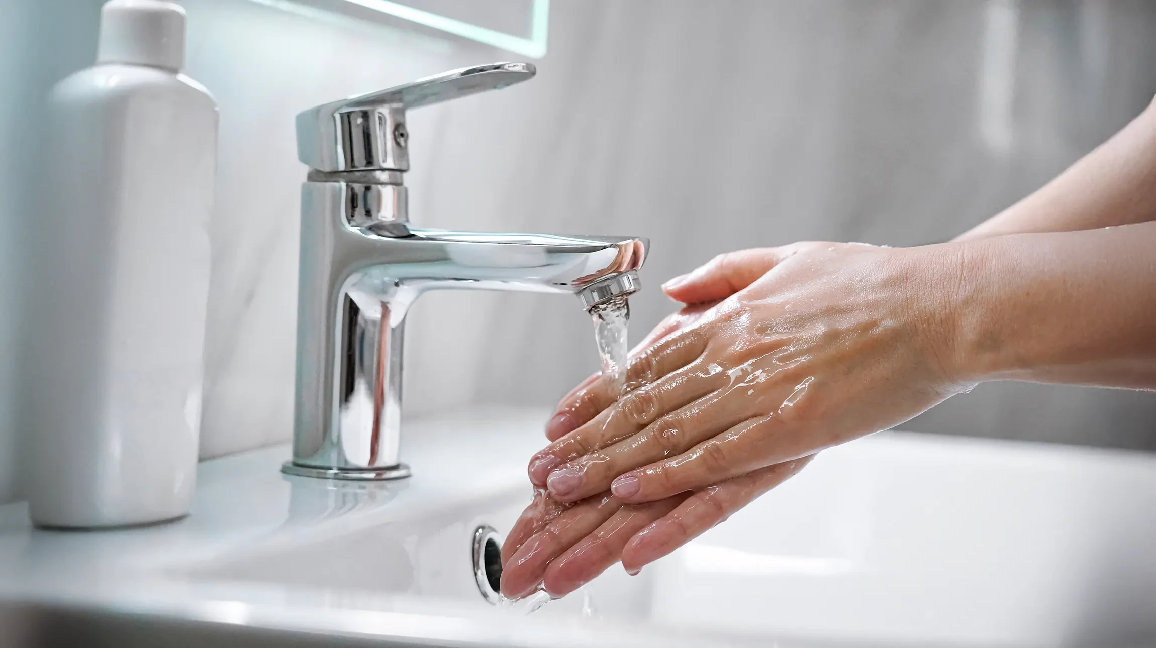 Plombier souriant en uniforme bleu travaillant sous &eacute;vier de cuisine, tenant tablette et montrant pouce lev&eacute;
